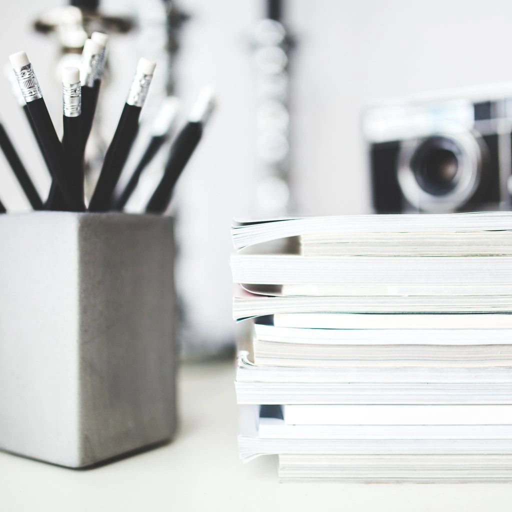 Overhead editorial shot of a stack of printed newsletters on a dark textured desk, one issue open with a highlighted column